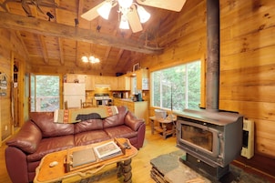 A cozy cabin interior with a leather sofa, a small wooden table, a fireplace, and a kitchen area.