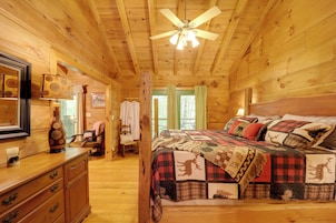 A wooden cabin interior with a bed, dresser, and a ceiling fan.