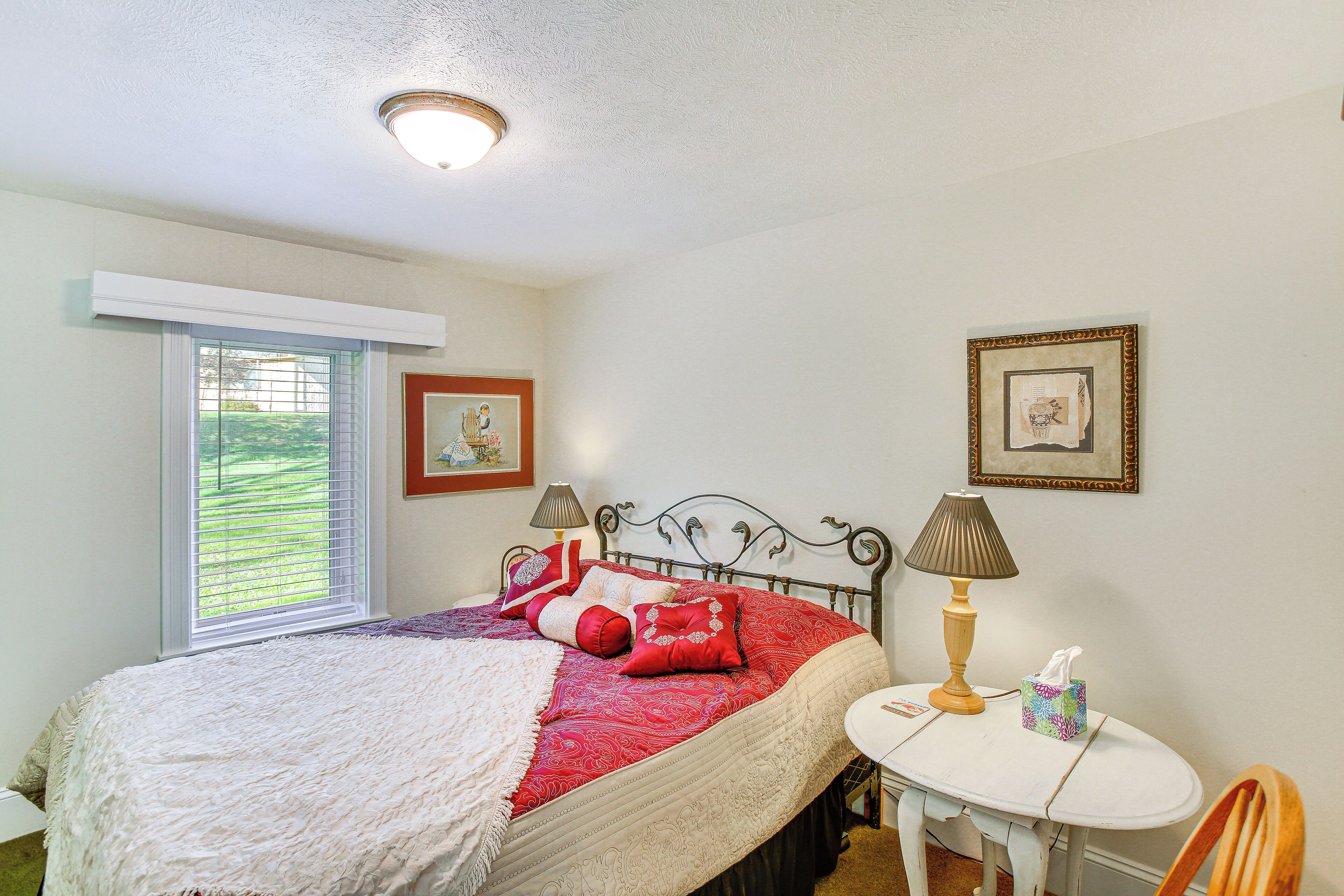 A neatly made bed with a red and white bedspread, a bedside lamp, and a small table with a tissue box.
