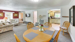 A spacious living room with a dining area, a TV mounted on the wall, and a kitchen visible through an open door. - Relax Fireside! Frankfort Apt Near Dtwn & Beaches (Frankfort)