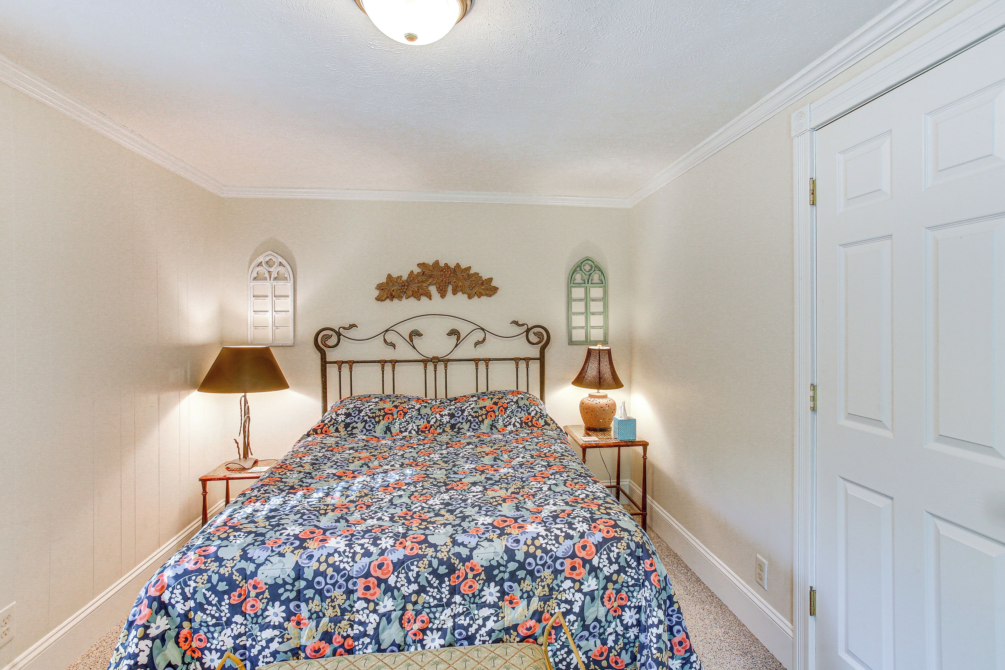 A bedroom with a floral bedspread, two bedside lamps, and a decorative wall piece.