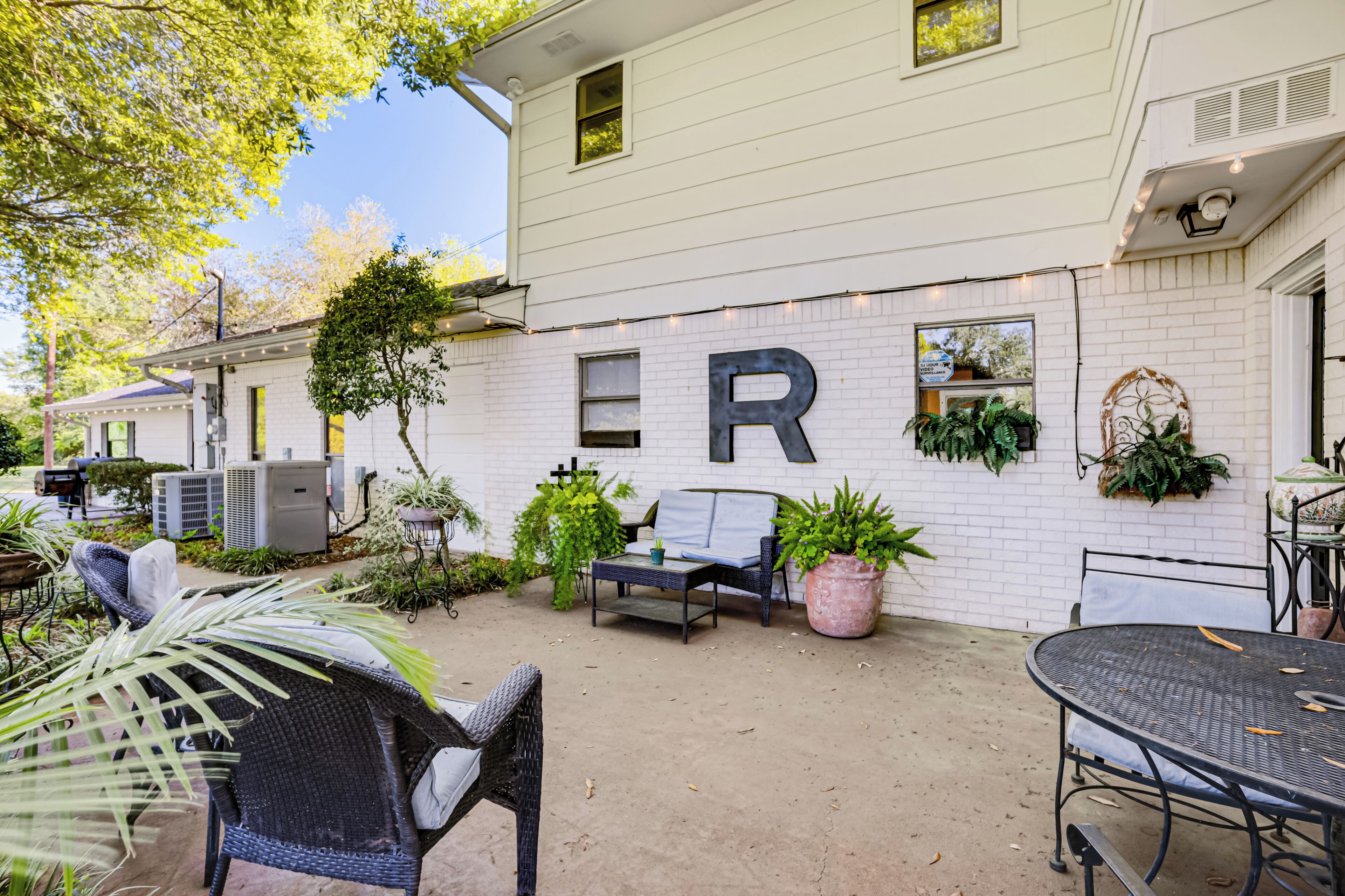 A white building with a large 'R' on the wall, outdoor seating, and potted plants.