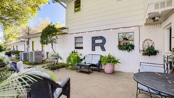 A white building with a large 'R' on the wall, outdoor seating, and potted plants.