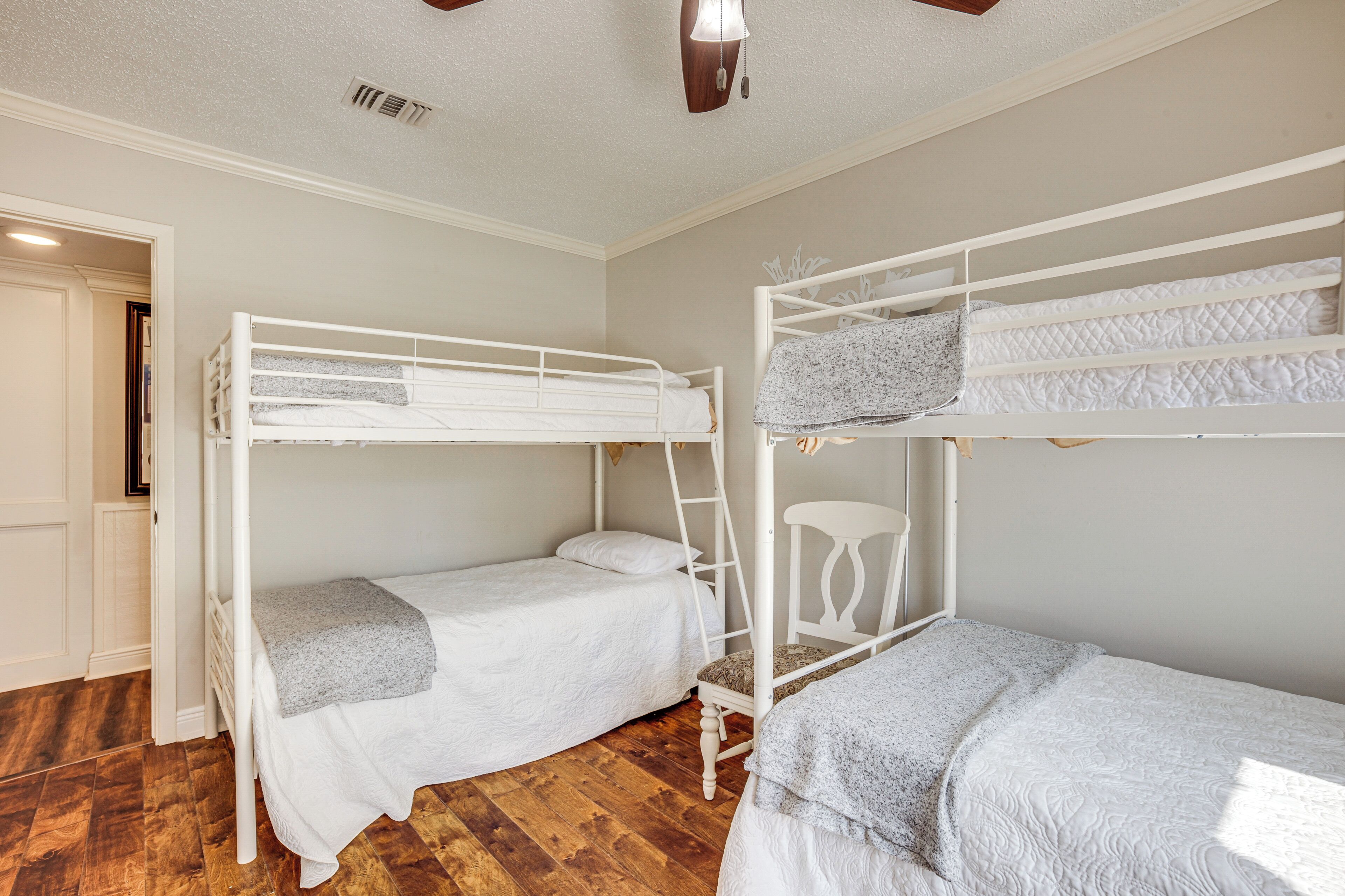 A room with two bunk beds, wooden flooring, and a white door.