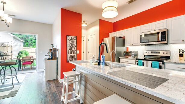 A modern kitchen with white cabinets, a large island, stainless steel appliances, and a bright red accent wall. - Canton Home w/ Fenced Yard: 6 Mi to Lake Allatoona (Canton)
