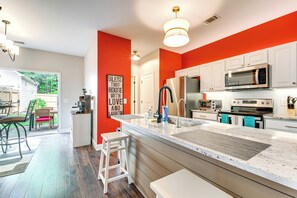 Een moderne keuken met witte kasten, een groot eiland, roestvrijstalen apparatuur en een felrode accentmuur.