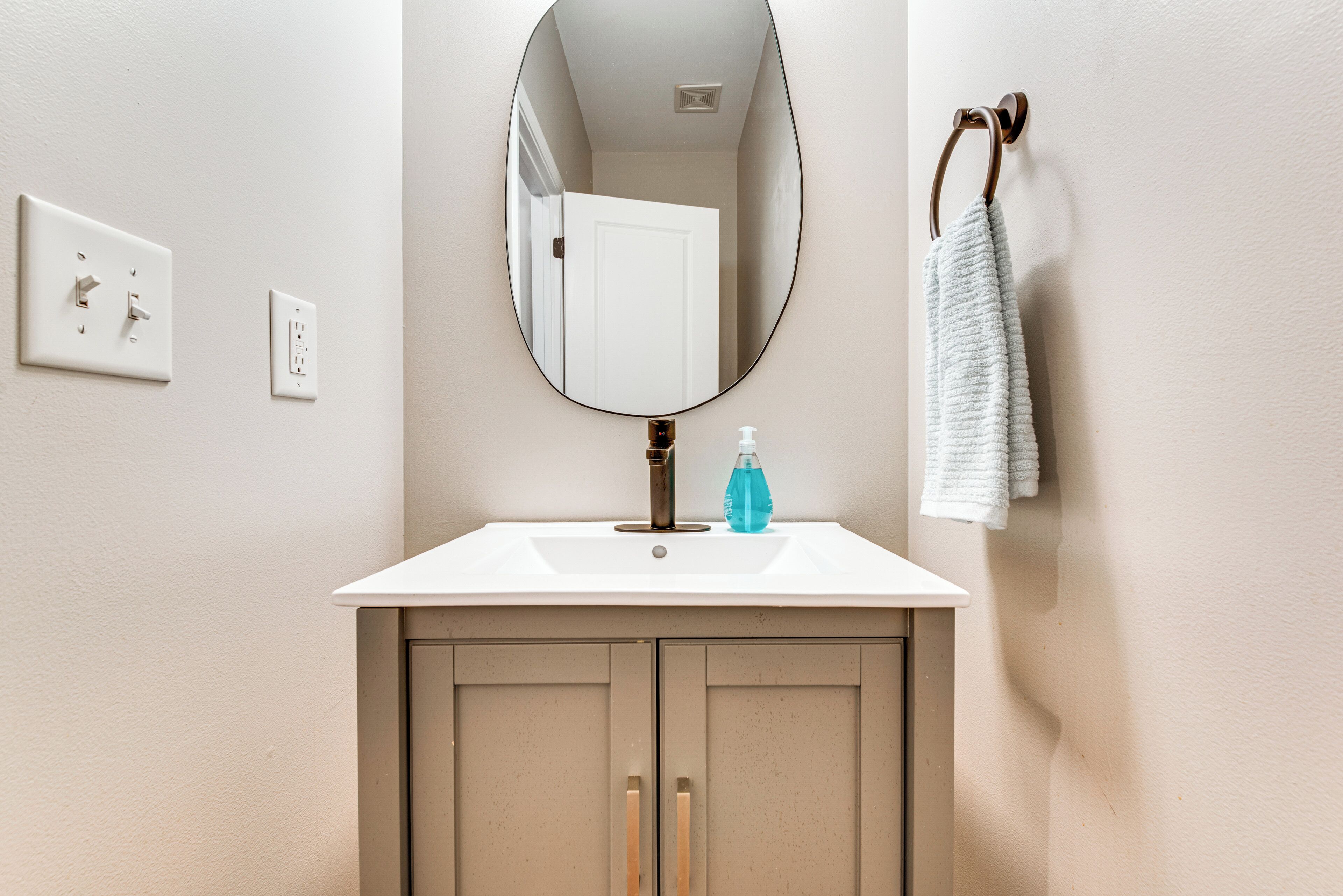 A bathroom with a white sink, a mirror, a towel rack, and a door.