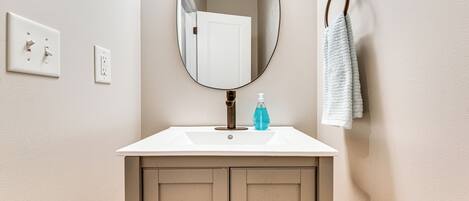 A bathroom with a white sink, a mirror, a towel rack, and a door.