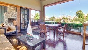 A spacious patio with a stone fireplace, wooden furniture, and a large glass door leading to a scenic view.