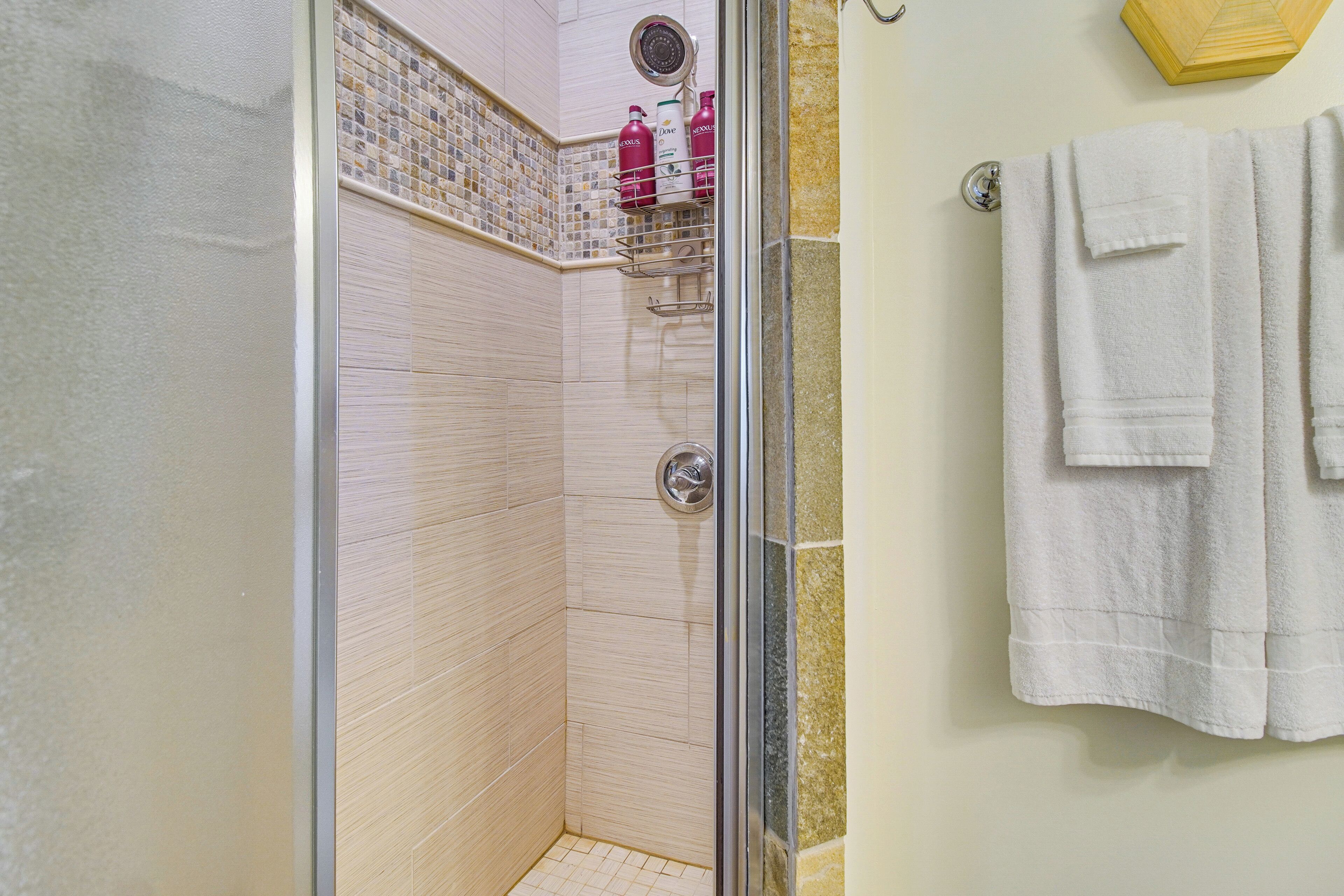 A bathroom with a shower area, a tiled wall, and a towel rack with towels.