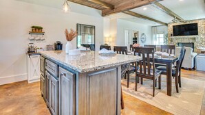 A spacious kitchen with a large island, wooden beams, and a stone fireplace.