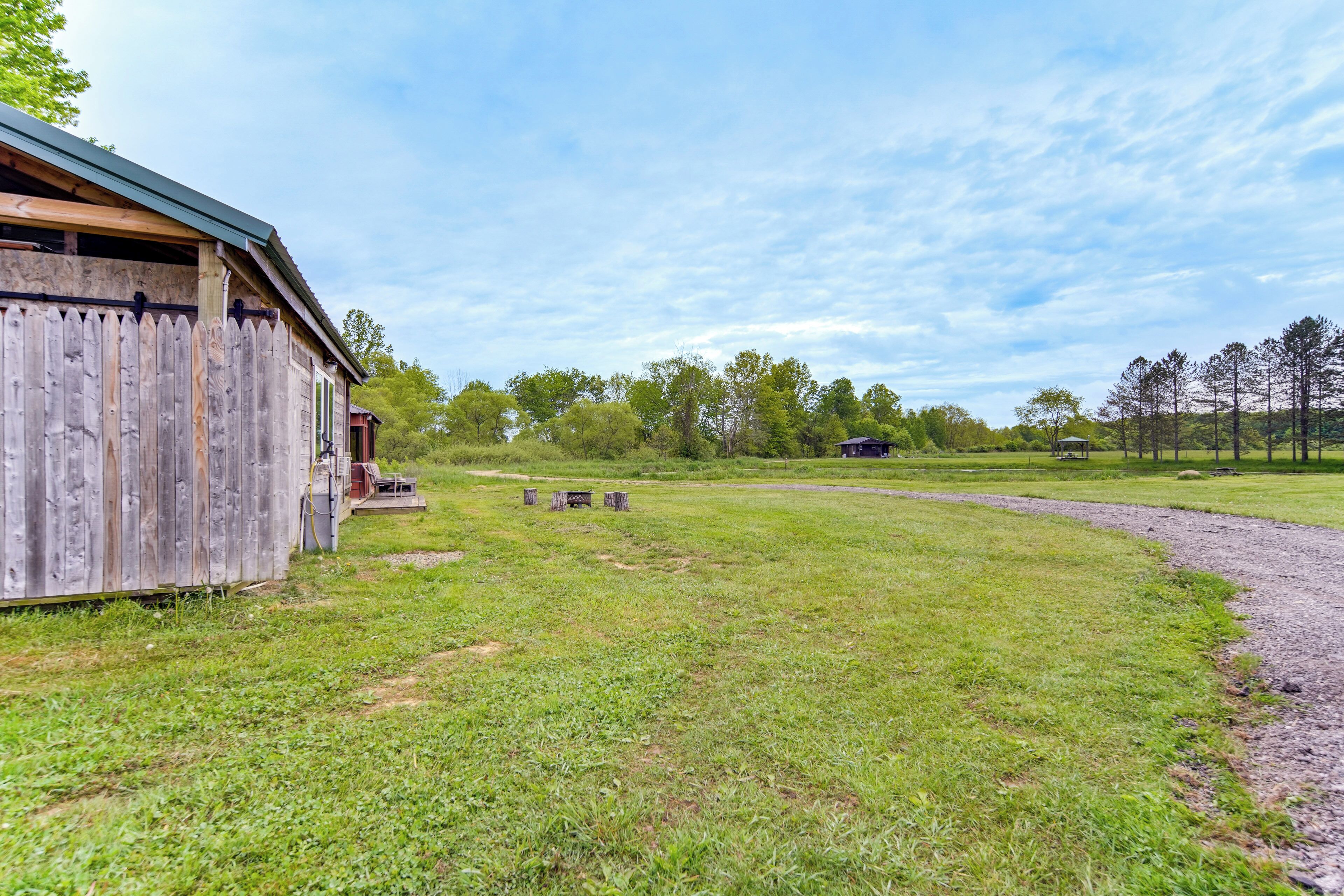 A rustic wooden building with a green roof, a grassy field, and a dirt path leading to a distant structure.