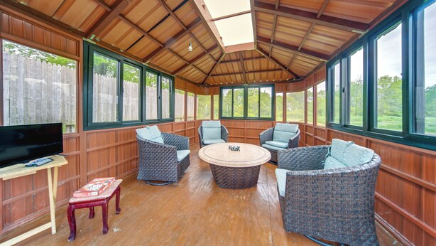 A covered outdoor seating area with wicker furniture, a central round table, and a television on a table. - Dog-friendly Cabin Near Pymatuning Lake! (Kinsman)