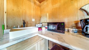 A compact kitchen with a white countertop, a microwave, a coffee maker, and wooden cabinets. - Dog-friendly Cabin Near Pymatuning Lake! (Kinsman)