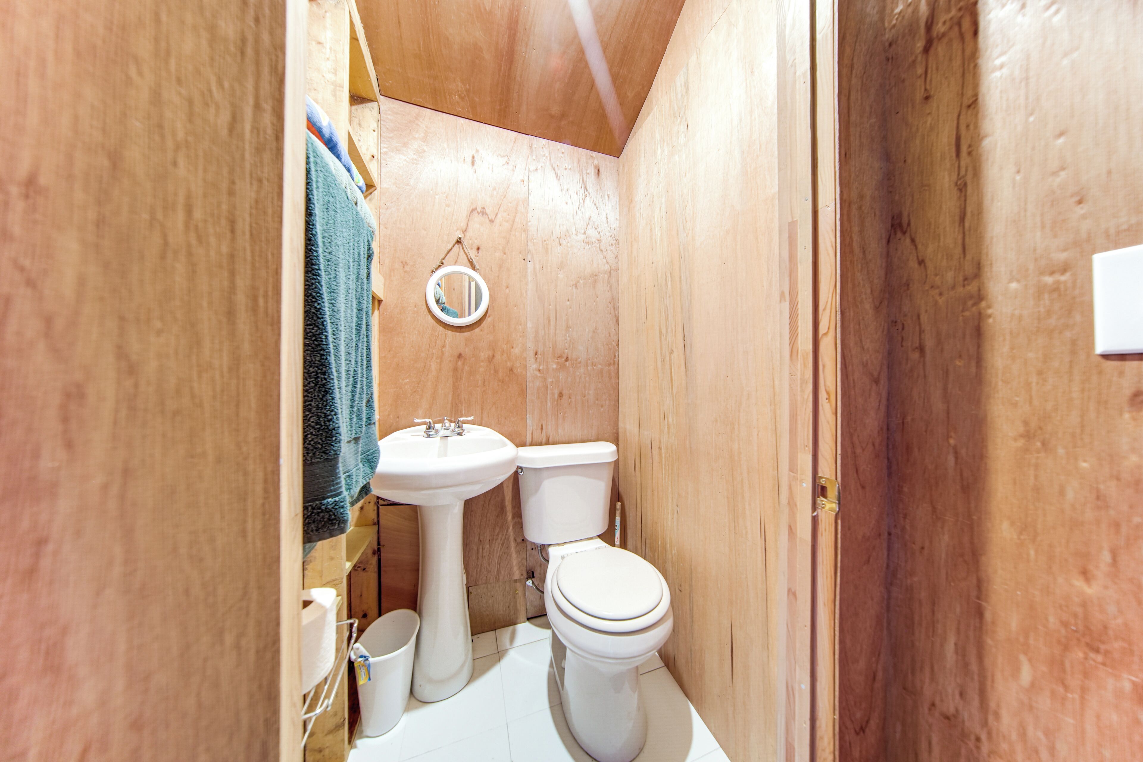 Un baño pequeño con paneles de madera, un lavamanos blanco, un inodoro y un espejo.