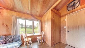 A wooden interior with a dining table, chairs, a sofa, and a large window offering a view of greenery. - Dog-friendly Cabin Near Pymatuning Lake! (Kinsman)