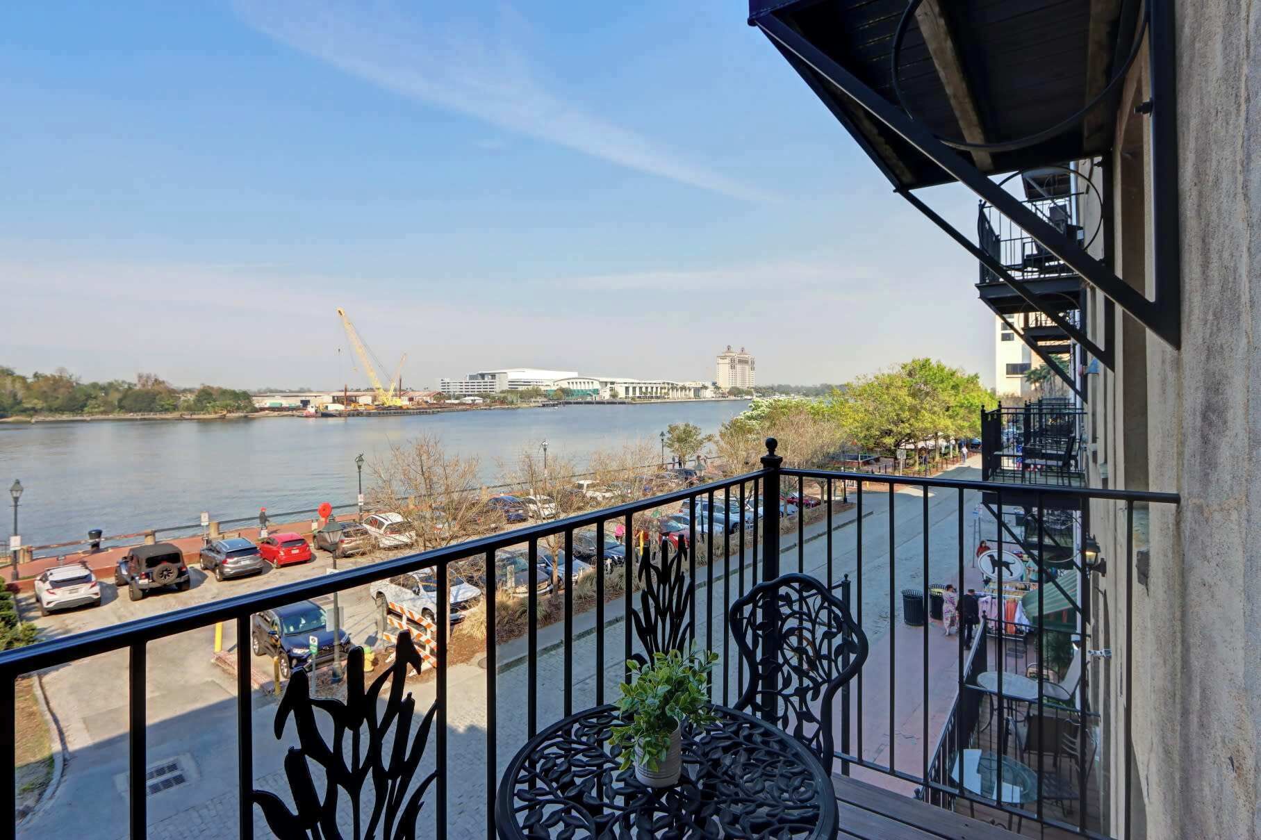 Un balcon avec vue sur une rivière, des voitures garées et un pont situé au loin.