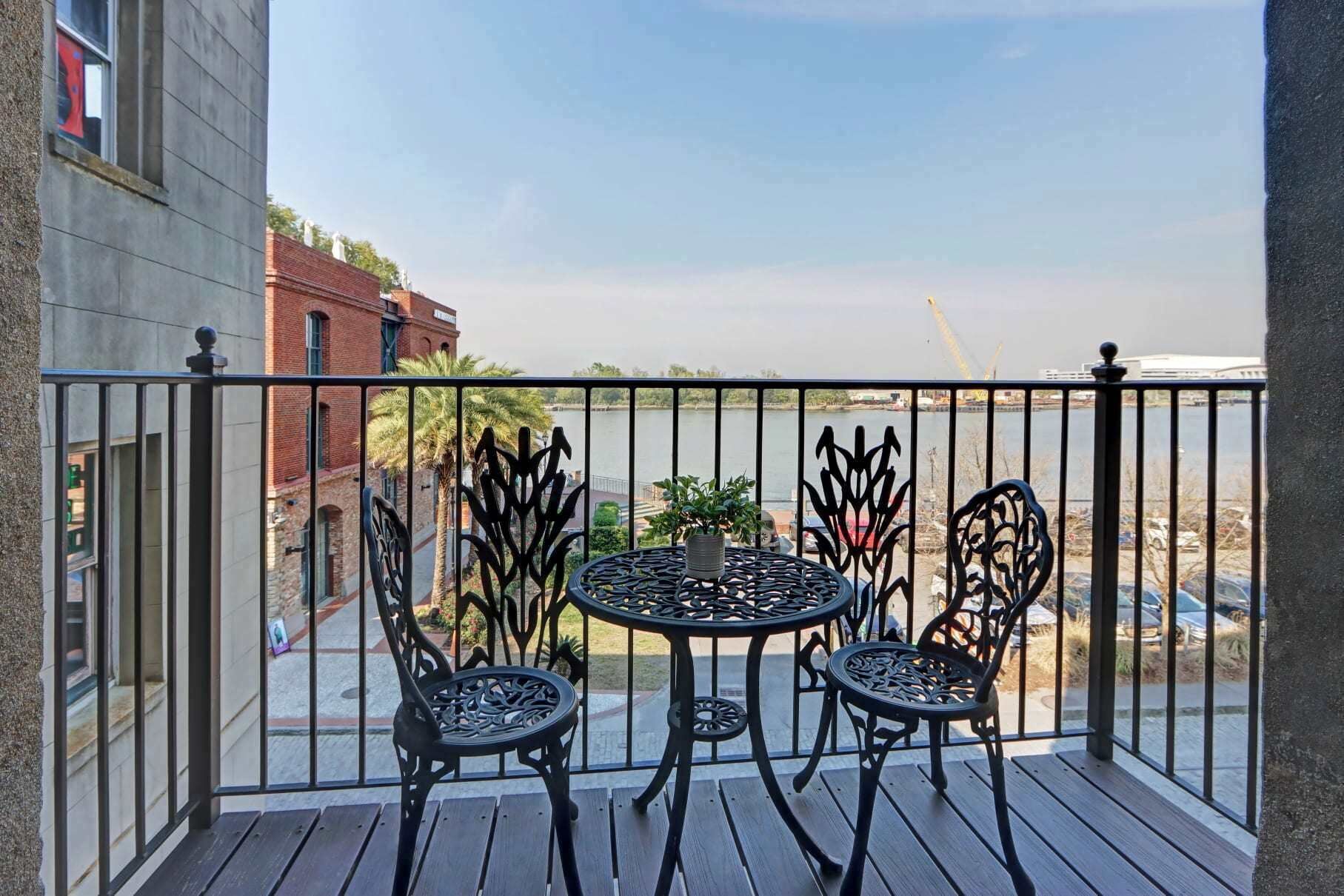 Ein Balkon mit Tisch und Stühlen, der auf ein Gewässer und Gebäude blickt.