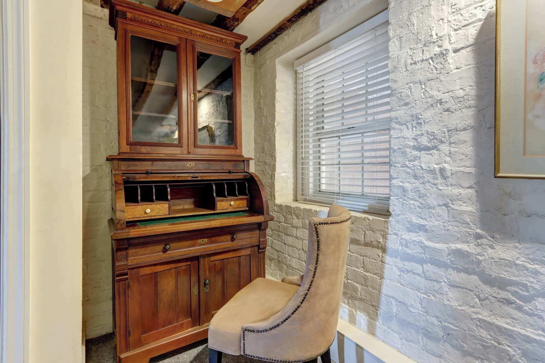 Une pièce d’angle avec un meuble en bois, une chaise, une fenêtre avec des stores et un mur à texture.