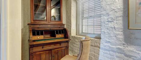 Une pièce d’angle avec un meuble en bois, une chaise, une fenêtre avec des stores et un mur à texture.