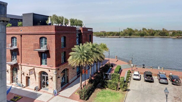 A brick building with a water view, a parking lot, and a statue on the roof. - The Riverfront Loft, Charming | River Views (Savannah)