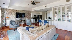 A living room with a sofa, chairs, a TV, and a kitchen in the background. - The Riverfront Loft, Charming | River Views (Savannah)