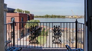 A balcony with a view of a river, a brick building, and a construction crane in the distance. - The Riverfront Loft, Charming | River Views (Savannah)