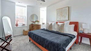 A bedroom with a bed, dresser, mirror, and artwork on the walls. - A Manor of State, Luxurious | Central | Modern (Savannah)