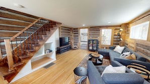 A modern living room with a wooden staircase, a grey sofa set, a TV, and a small dining area. - Rustic & Refined - Gunnison (Gunnison)