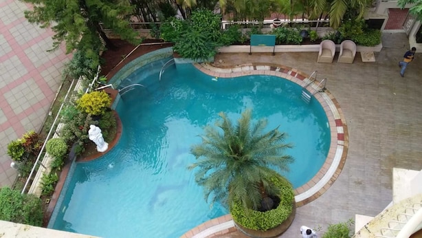 A circular pool with a palm tree in the center, surrounded by a tiled deck and various plants. - Kailash Parbat (Mawal)