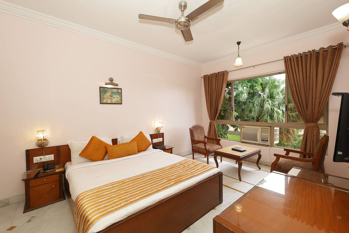 Habitación de hotel con cama, dos mesitas de noche, escritorio, silla, ventilador de techo y ventana con cortinas.