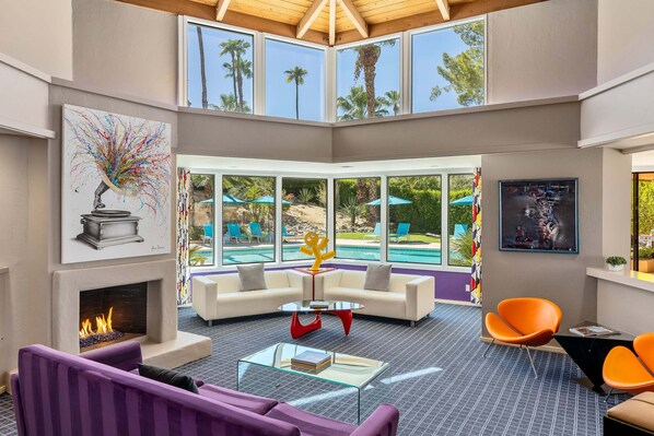 A spacious living area with a fireplace, white sofas, a glass coffee table, and a pool view.