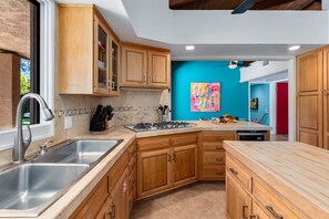 A kitchen with wooden cabinets, a stainless steel sink, a gas stove, and a colorful painting on the wall.