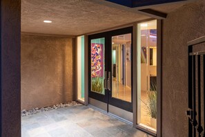 A hallway with a textured wall, a glass door with a colorful artwork, and a tiled floor.