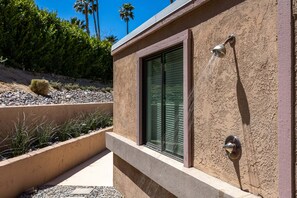 A modern building with a window, a wall-mounted shower, and a landscaped area with rocks and plants.