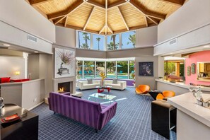 A spacious living area with a high ceiling, large windows, a fireplace, and modern furniture.