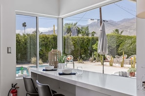 A modern kitchen with large windows, a pool view, and outdoor seating.