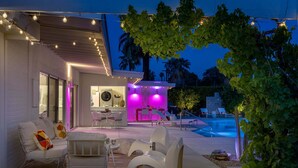 A modern outdoor living area with a pool, seating, and ambient lighting. - Desert Bloom Retreat - Upscale Mid-Mod Home! (Palm Springs)