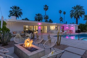 Ein modernes Haus mit Pool, Sitzgelegenheiten im Freien und einer Feuerstelle.