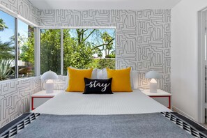 Ein modernes Schlafzimmer mit einem großen Bett, zwei Nachttischlampen, Blick ins Grüne und einer Wand mit Muster.