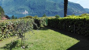 Ein üppiger Garten mit einer Palme, einer Hecke und Blick auf einen See und Berge.