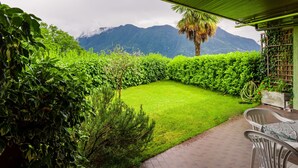 Eine Terrasse mit Blick auf Berge, eine Rasenfläche und eine Pergola.
