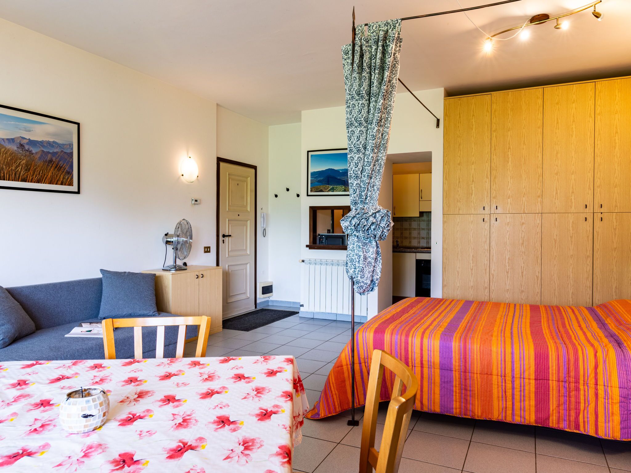 A cozy room with a bed, a sofa, a dining table, and a kitchen area visible through an open door.