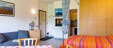 A cozy room with a bed, a sofa, a dining table, and a kitchen area visible through an open door.