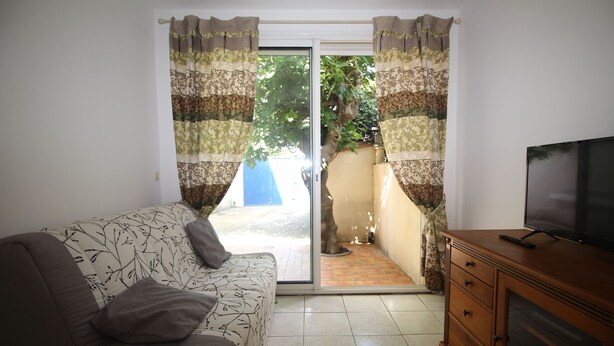 Un salon comprenant un canapé, un téléviseur posé sur un meuble en bois et une porte-fenêtre coulissante donnant sur un espace extérieur.
