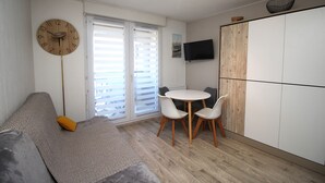 A modern living room with a sofa, a dining table with chairs, a clock, and a TV mounted on the wall. - Studio for 4 with marina view (Canet-en-Roussillon)