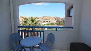 A balcony with a table and chairs, overlooking a pool and buildings. - Studio for 4 with marina view (Canet-en-Roussillon)