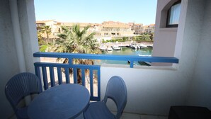 A balcony with a table and chairs, overlooking a marina with boats and buildings in the background. - Studio for 4 with marina view (Canet-en-Roussillon)