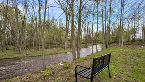 A bench by a river in a wooded area. - Serene Riverside Retreat 3 Bedroom Home by RedAwning (Little Suamico)