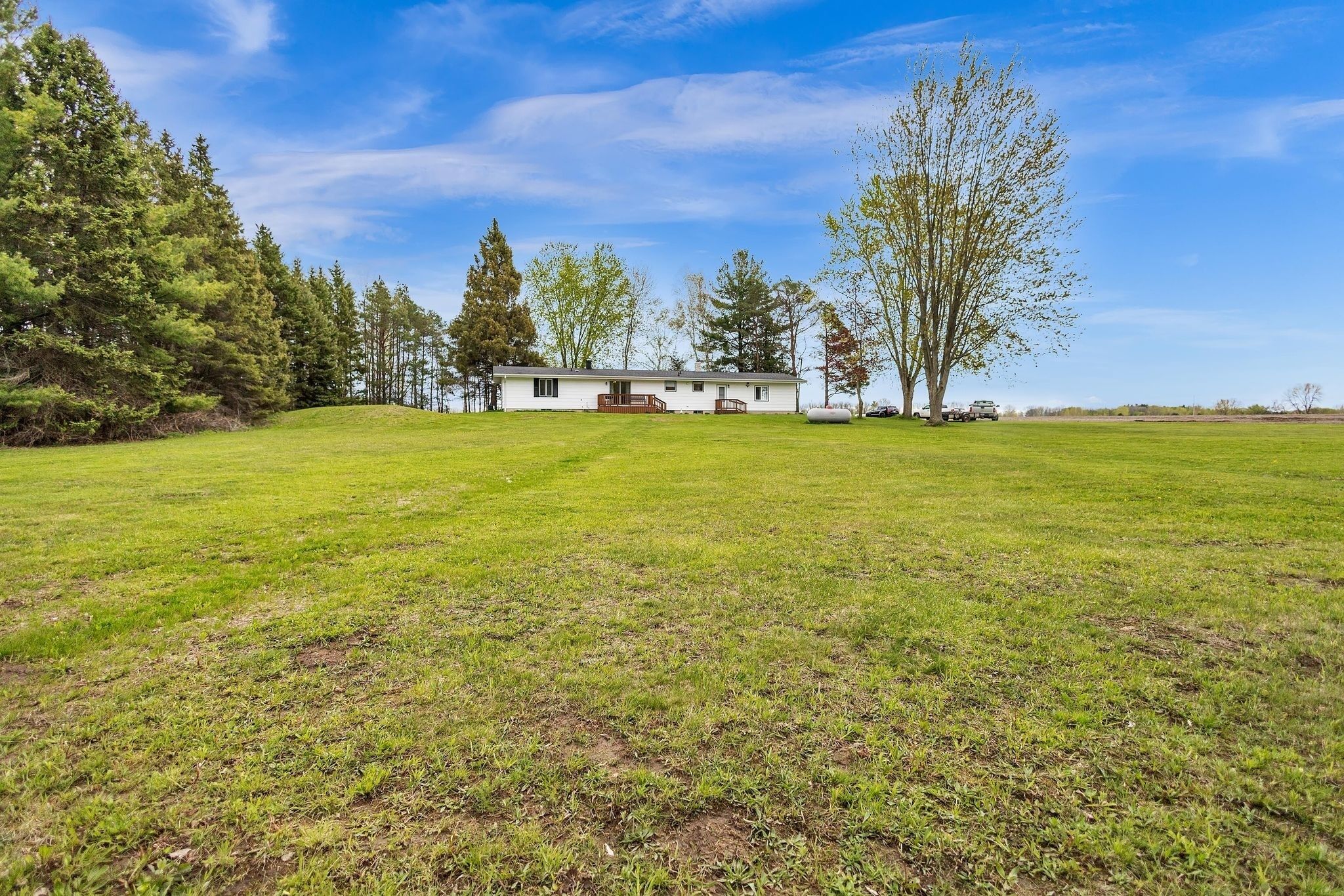 Eenlaags huis met een veranda, omringd door een groot grasveld en bomen.